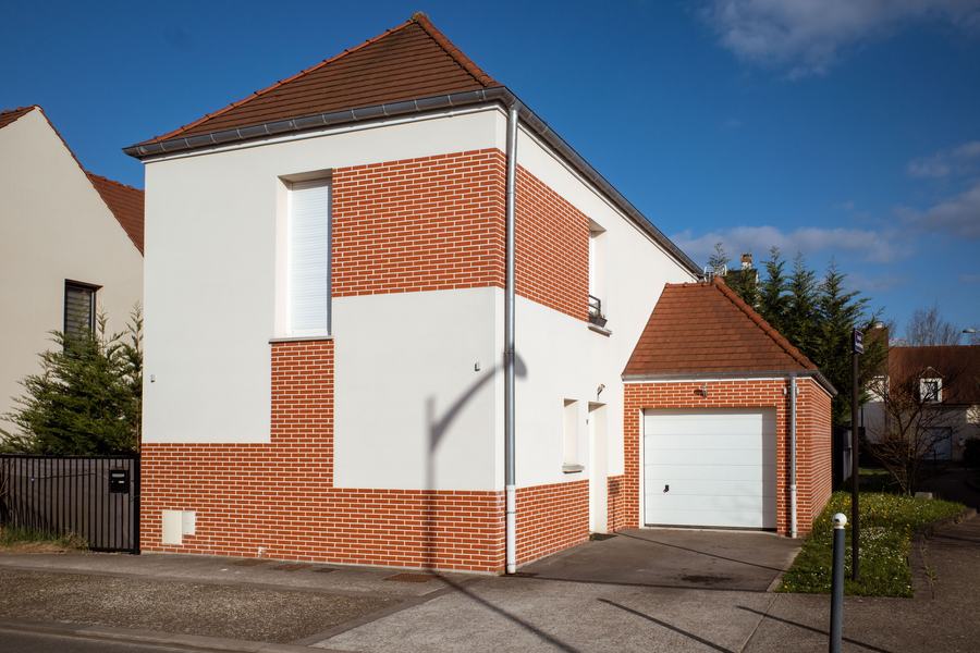 Maison à murs blancs et briques rouges avec un garage attenant